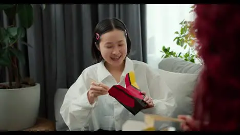 Young asian woman in good mood eats noodles with wood sticks at home with her friend