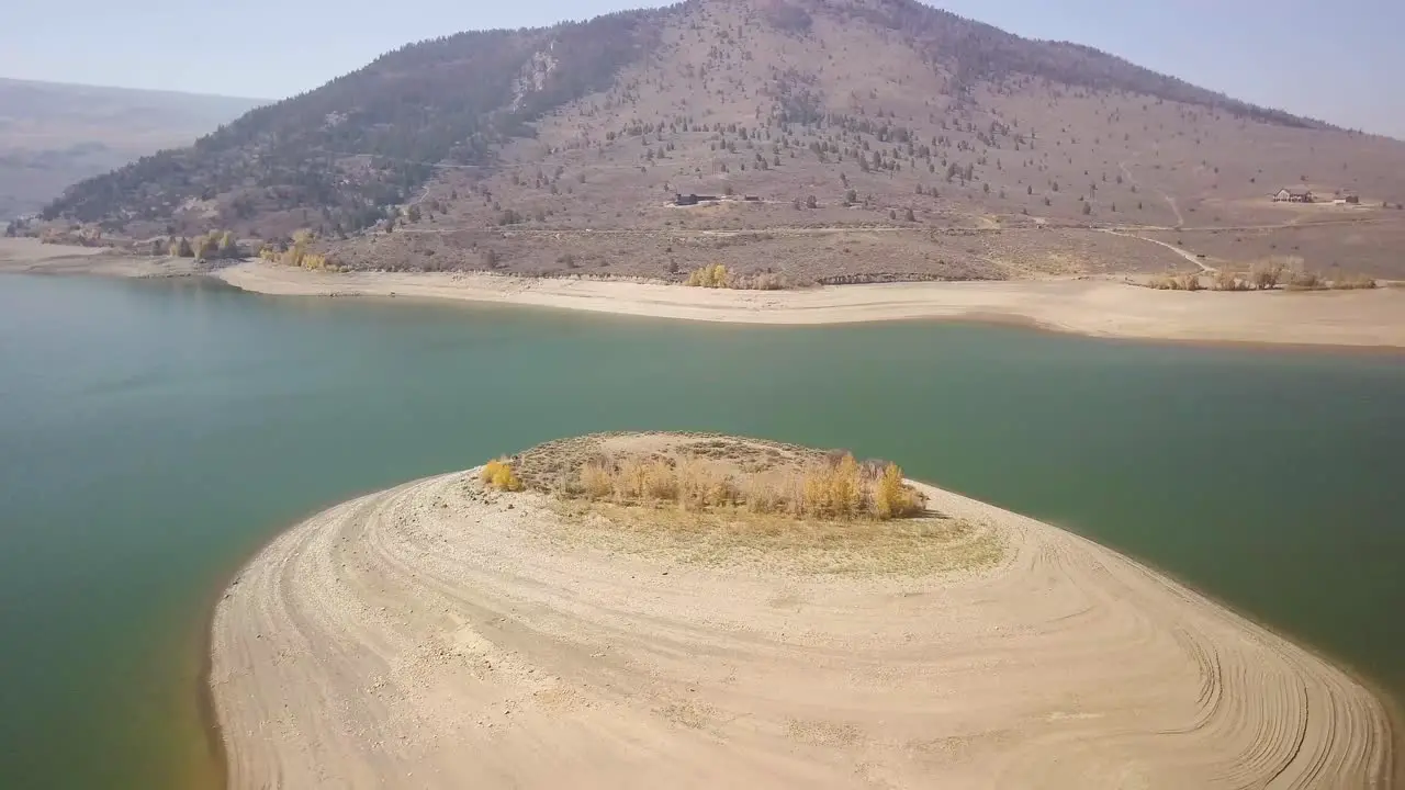 A trucking pan of an island attached to a dry lake bed with aspen trees and a bright blue sky