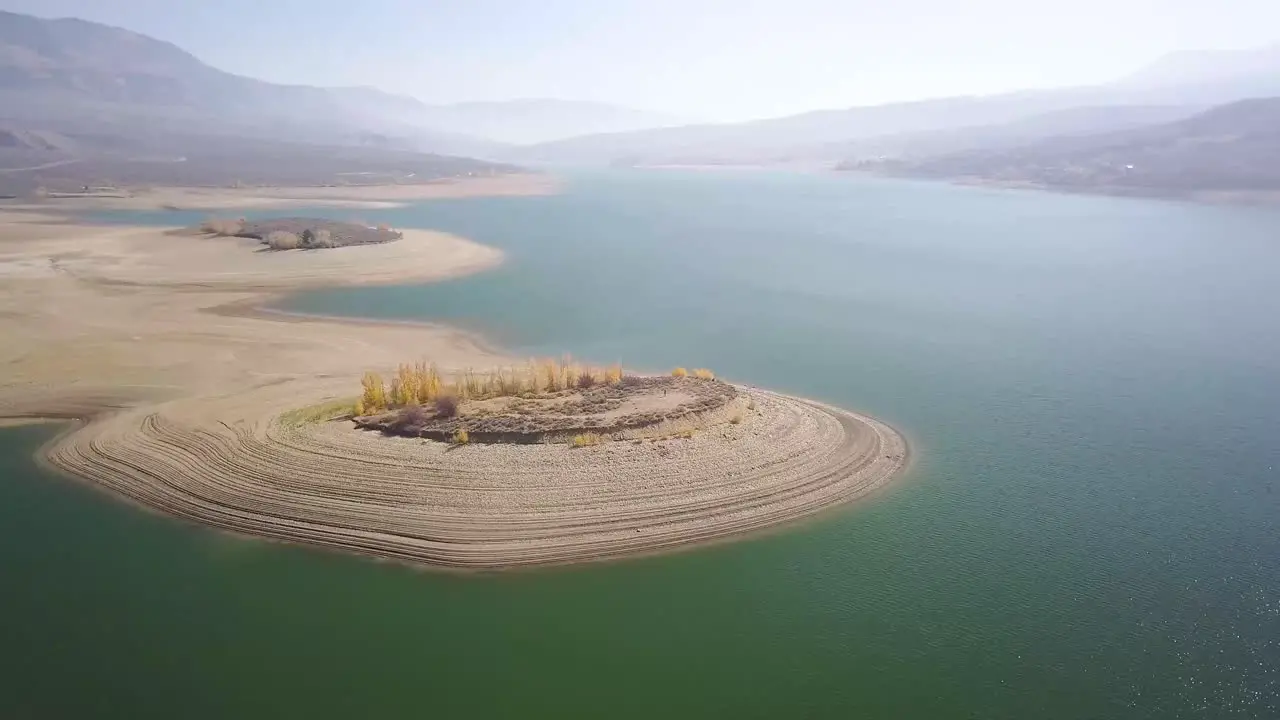 A trucking pan of an island in a semi-dry lake bed in Colorado with super dry conditions and beautiful mountain ridges with smoky haze