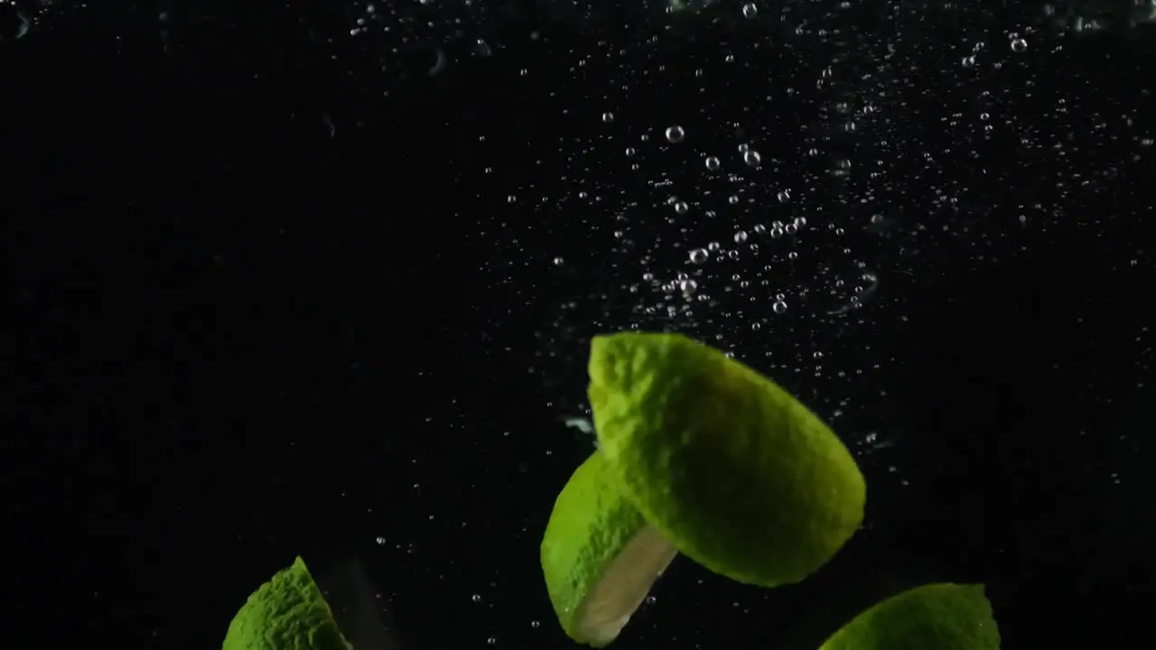 Lime citrus fruit isolated pieces of split and cut green lime dropping into water on a black background