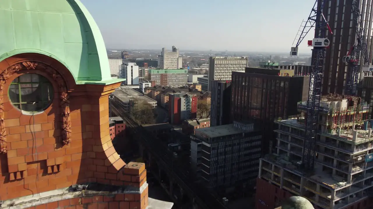 Arial drone flight passing by the green dome structure of the clock tower on the Kimpton Building on Oxford Road in Manchester City Centre with a view of new developments under construction