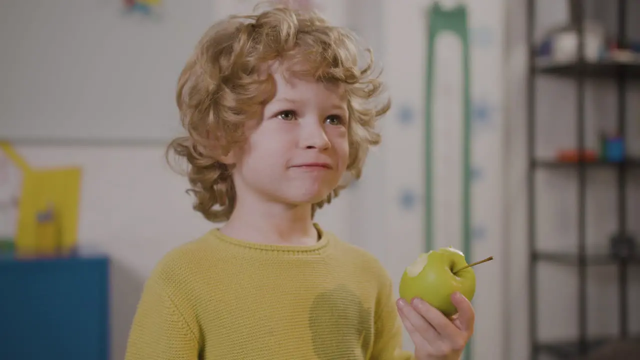 Little Boy Eating An Apple In Classroom In A Montessori School