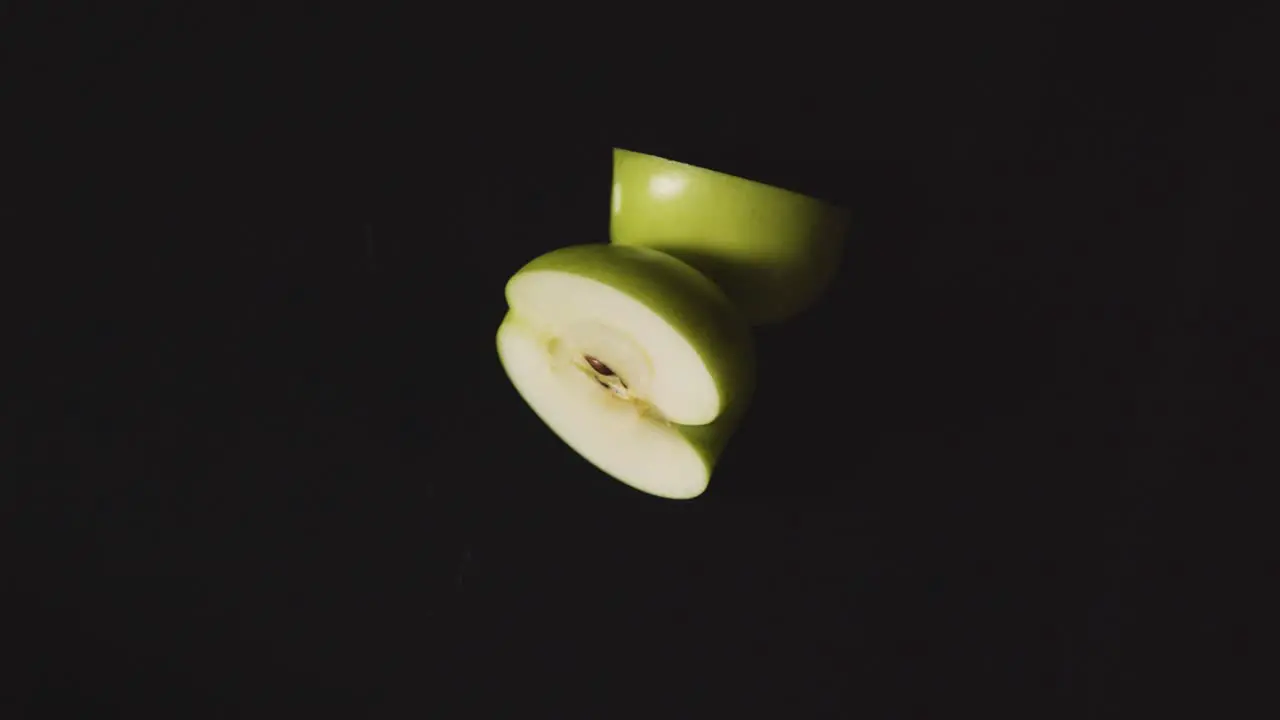 Overhead Studio Shot Of Halved Green Apple Revolving Against Black Background