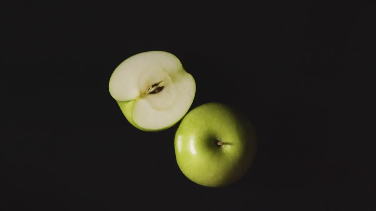 Overhead Studio Shot Of Whole And Halved Green Apple Revolving Against Black Background