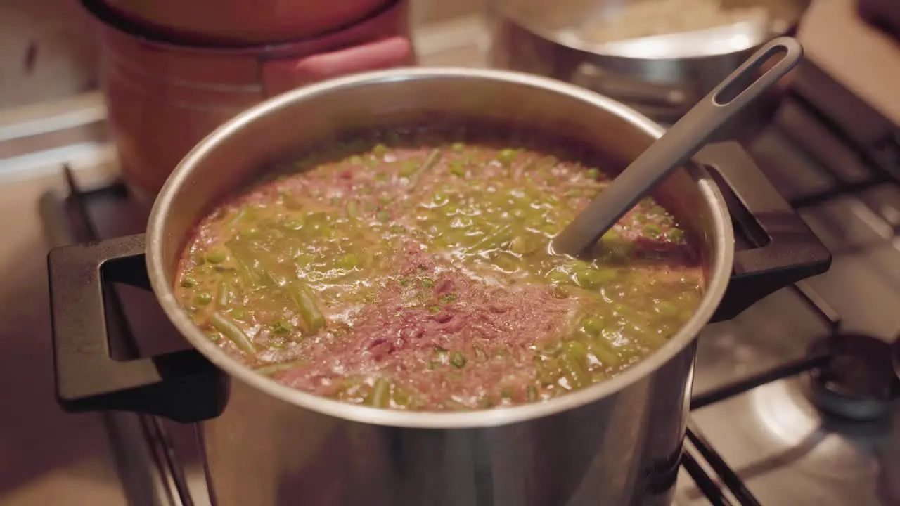 Soup boiling on gas stove in kitchen with ladle in the pot close up static shot