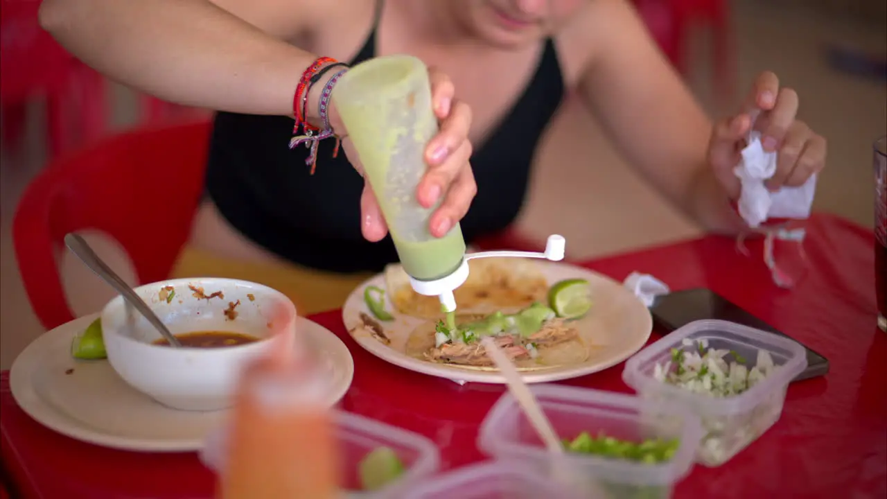 Slow motion close up of a latin woman preparing her barbacoa taco topping it with green chilli sauce in a restaurant in Mexico