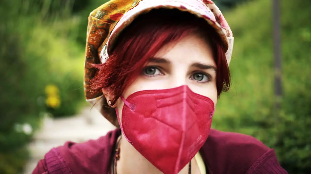 Idle Close-Up pan of a red haired vintage girl wearing her red medical face mask outdoor in the garden or park