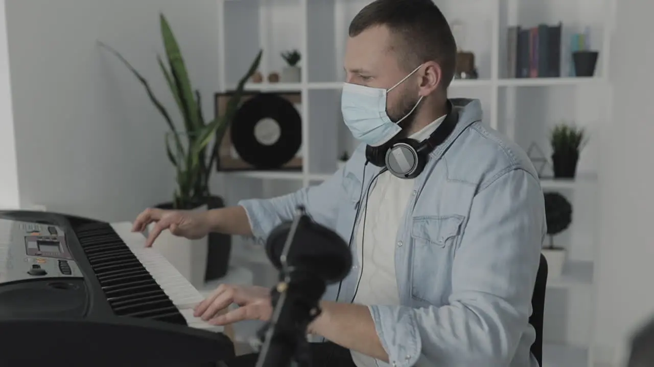 Male Musician With Medical Face Mask Playing Electric Keyboard At Home During Lockdown Due To The Covid 19 Pandemic