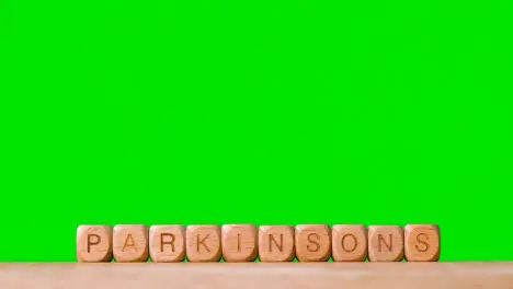 Medical Concept With Wooden Letter Cubes Or Dice Spelling Parkinson's Against Green Screen