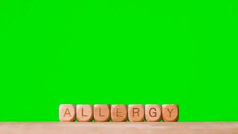 Medical Concept With Wooden Letter Cubes Or Dice Spelling Allergy Against Green Screen Background