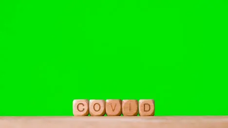 Medical Concept With Wooden Letter Cubes Or Dice Spelling Covid Against Green Screen Background