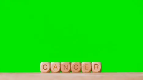 Medical Concept With Wooden Letter Cubes Or Dice Spelling Cancer Against Green Screen Background