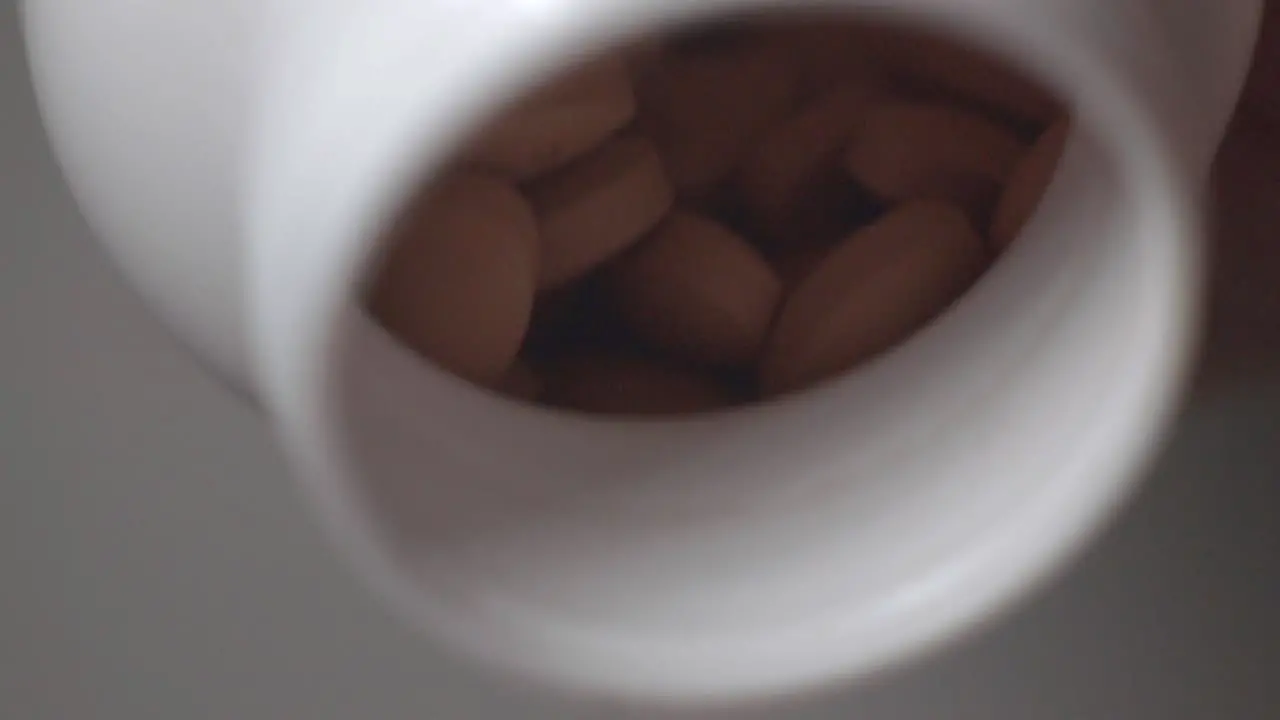 Brown Coated Pills Spilling Out From A White Bottle