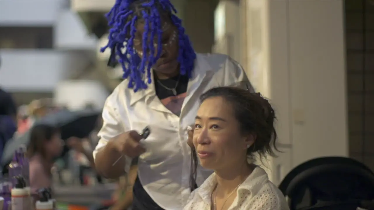 Asian woman getting fresh hairdo by African woman hair stylist at indoor ethnic cultural festival filmed as slow motion medium close up shot in handheld style