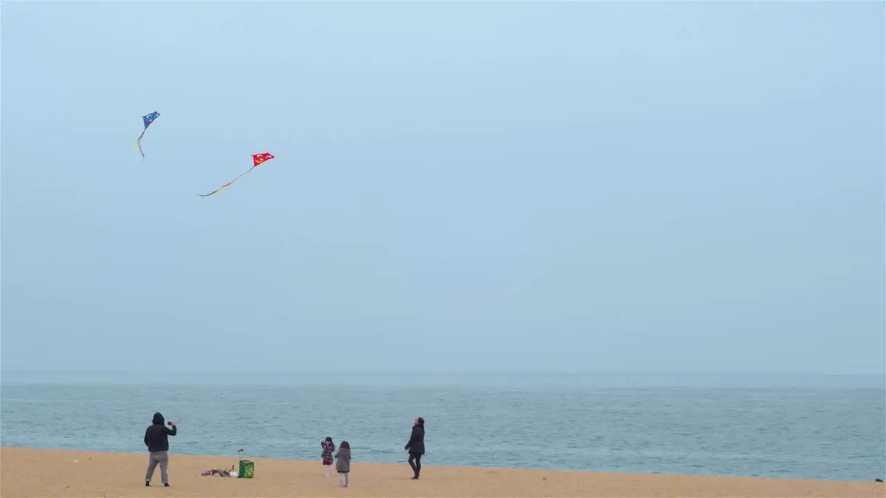 Family with children flying kites on the beach in Barcelona