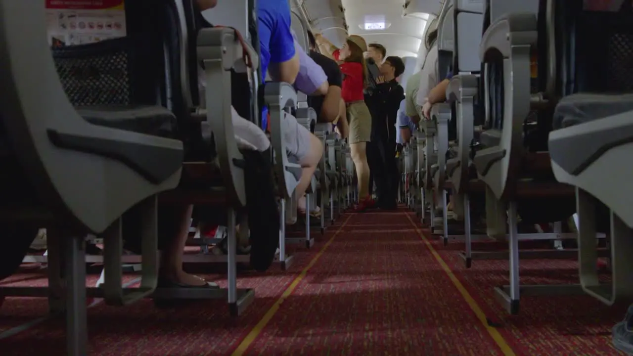 Flight attendant assists passengers stow luggage in overhead bins