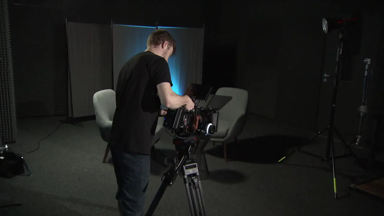 a person puts a red cinema camera on a tripod in a studio