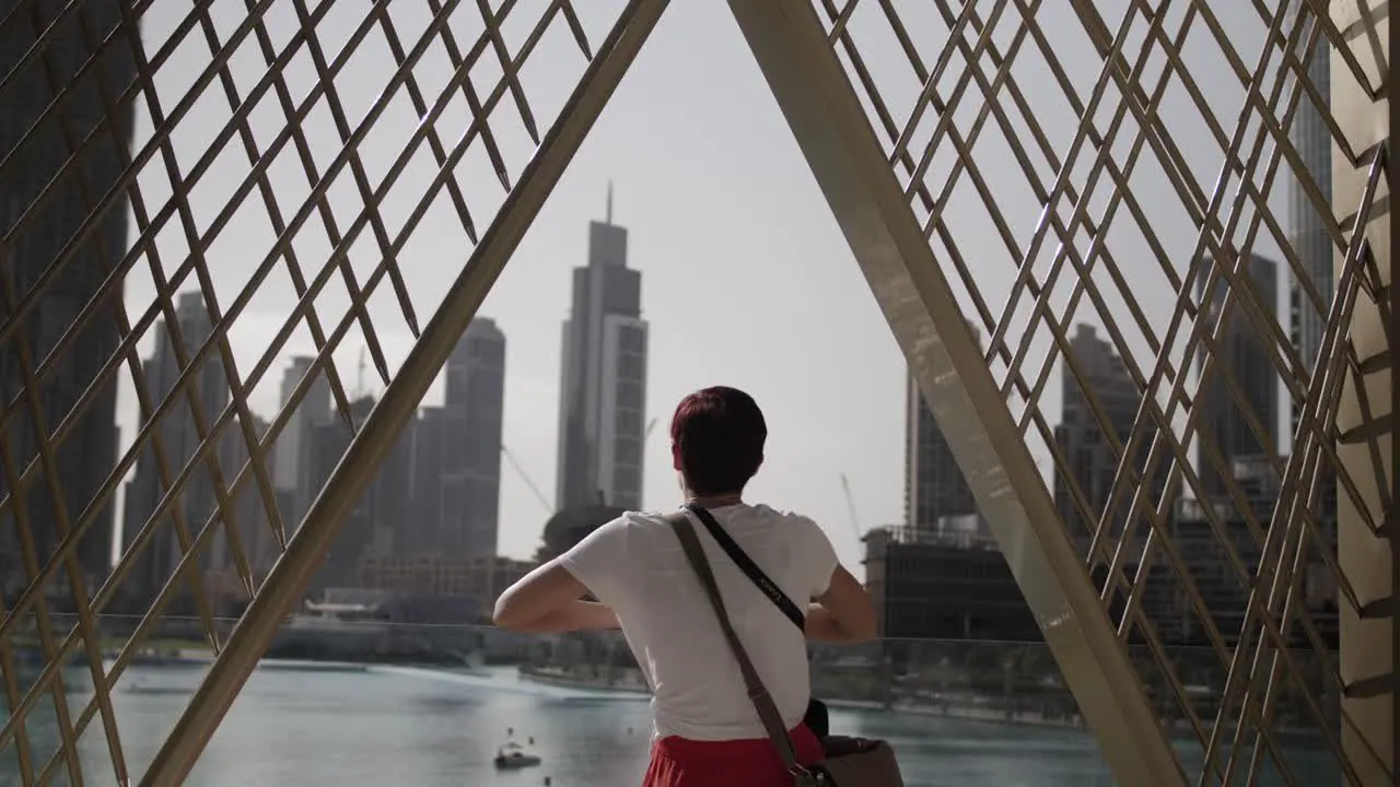 A woman stands on a balcony looking out at the city of Dubai with large buildings and skyscrapers in the distance