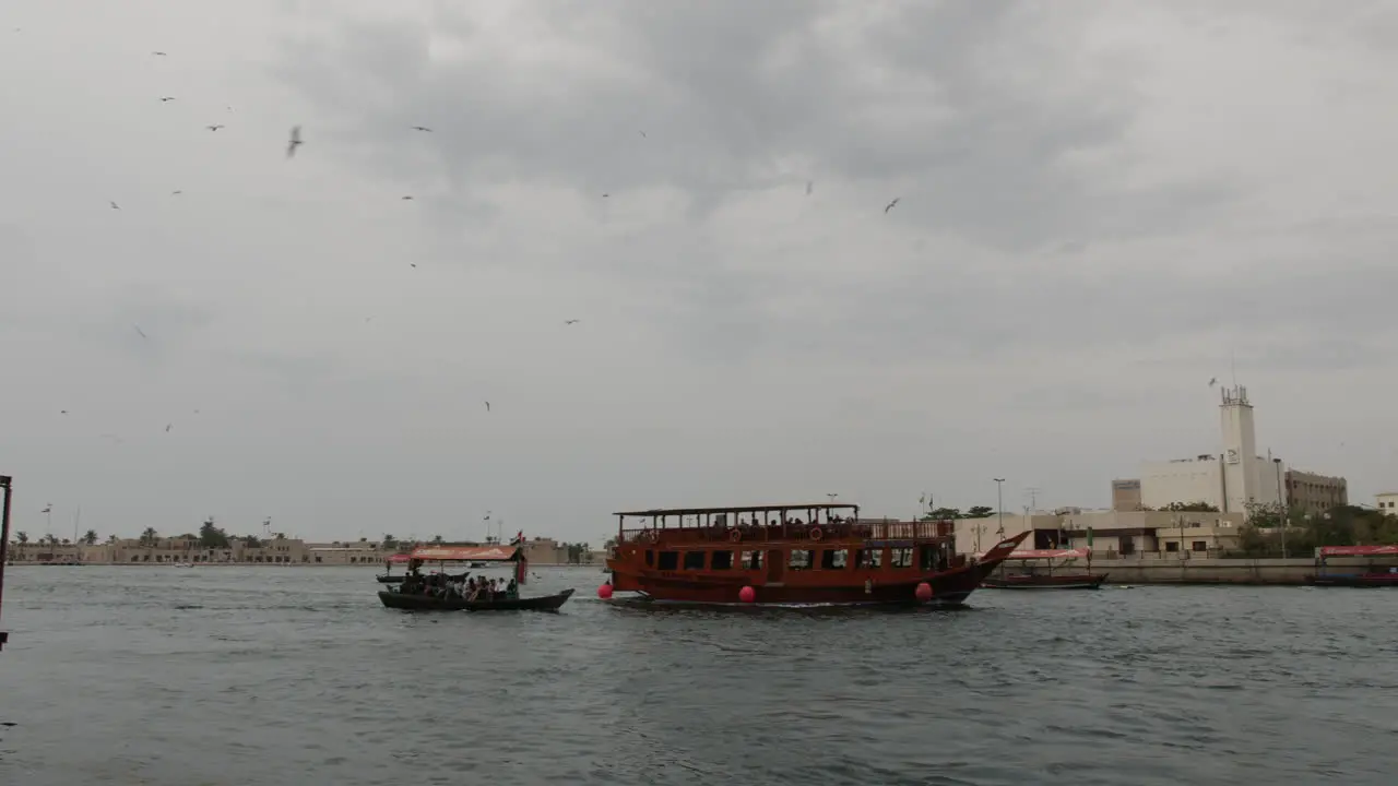 Middle eastern boats going down the river in Old Dubai on a cloudy and overcast day as Seagulls fly overhead in slow motion 60fps