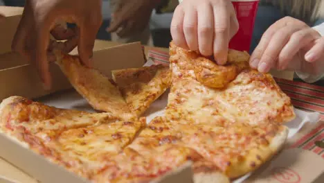 Multi-Cultural Friends Sitting On Sofa At Home Eating Takeaway Pizza Delivery 5