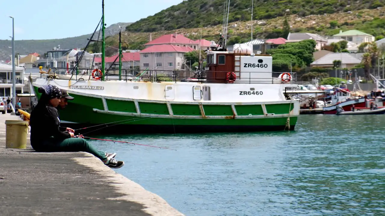 Casual South Africa couple sitting on Kalk Bay harbour wall fishing