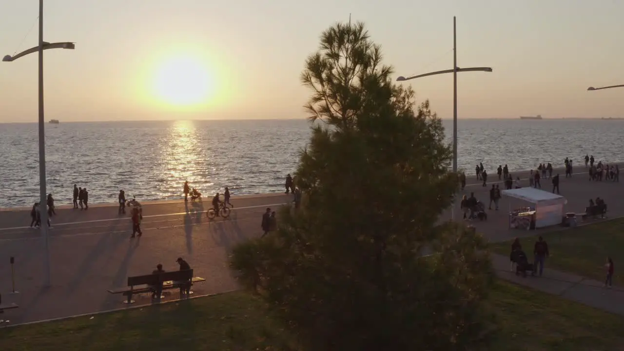 Aerial Low shot of people walking on Thessaloniki's seaside walkway at sunset