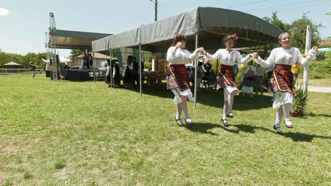 Young ladies in costume dance happily at Bulgarian summer folk festival