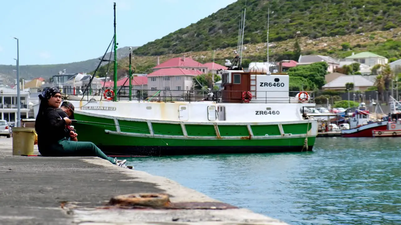 Casual contented couple sitting on Kalk Bay harbour wall relaxing fishing