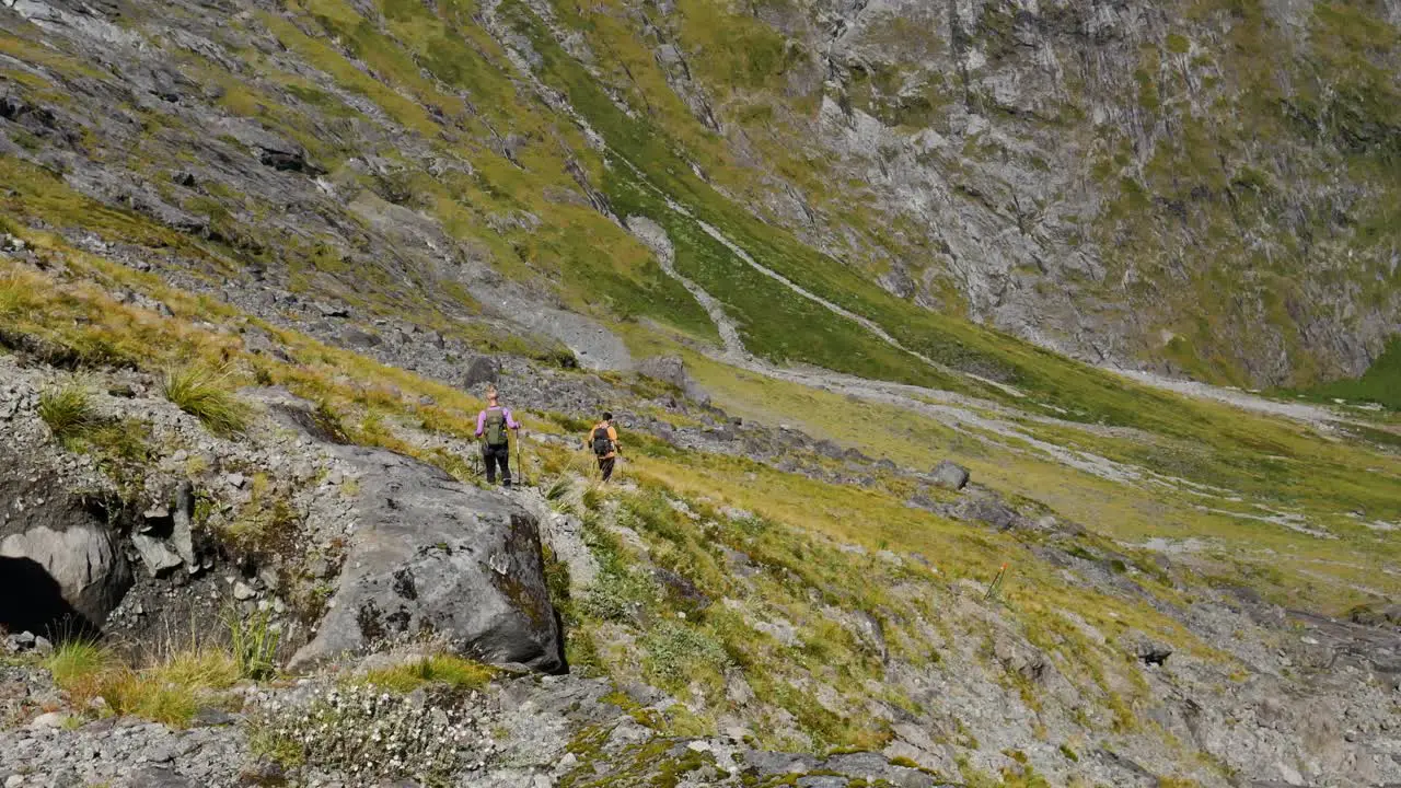 Pan shot of hiker couple hiking downhill steep green mountains on during sunny day at Gertrude Saddle