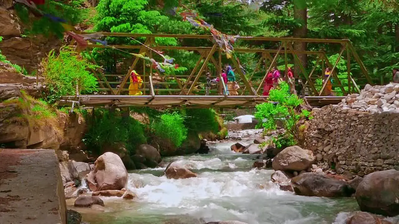 Cinematic Slo-Mo shot of people crossing bridge over Ganges river crystal clear water flowing downstream from mountains in harshal village of uttarakhand