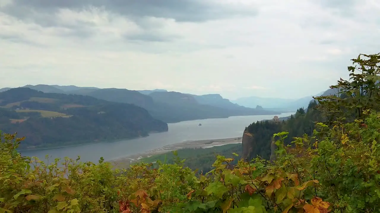 HD Boom up with autumn colored hedges in foreground and the Vista House on a cliff in the distance overlooking the Columbia River with mostly cloudy sky take one