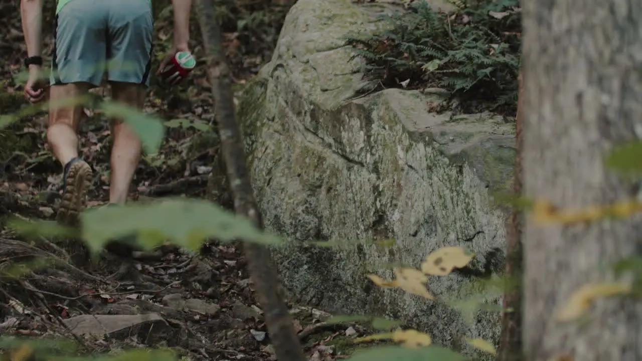 Man is hiking in the woods climbing over steep terrain and going up hills