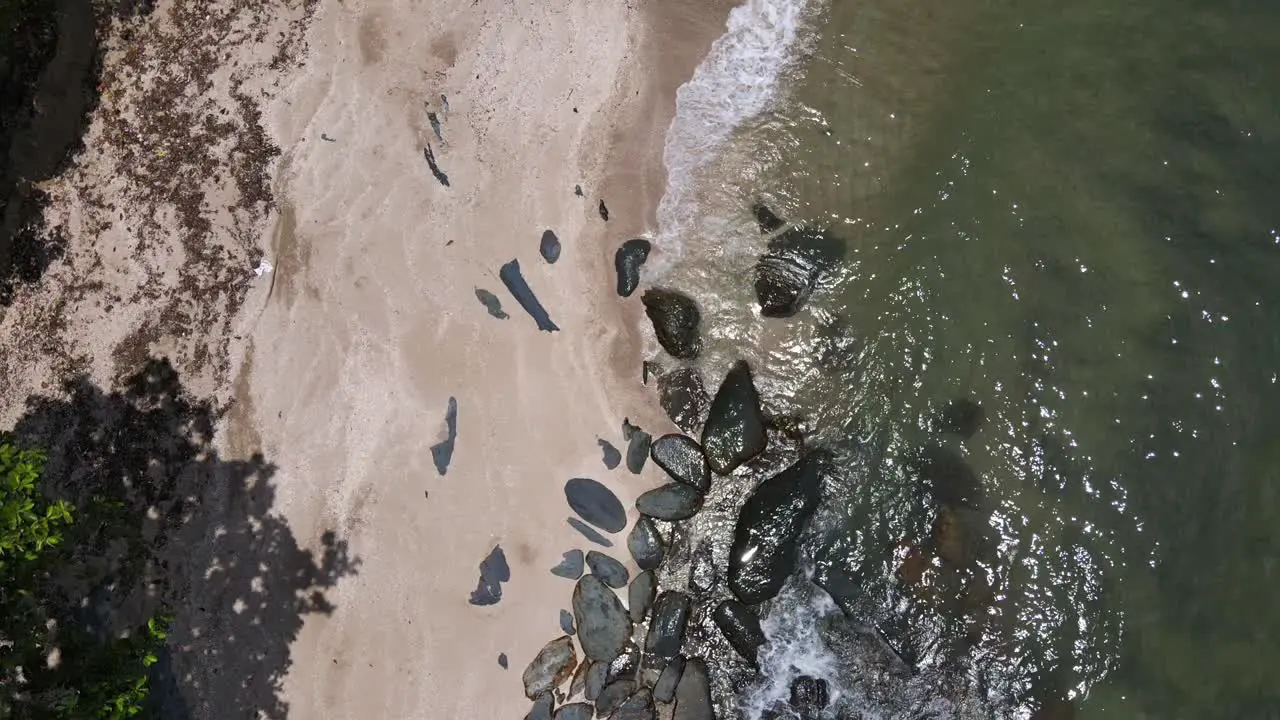 drone vertical tracking shot of jungle beach and ocean with granite rocks