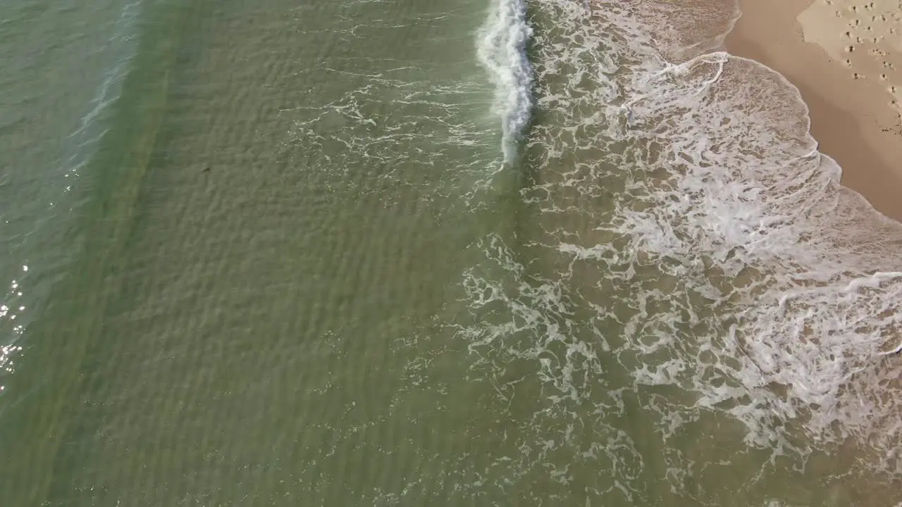 Drone Pan shot of small waves breaking on white sand beach with clear water