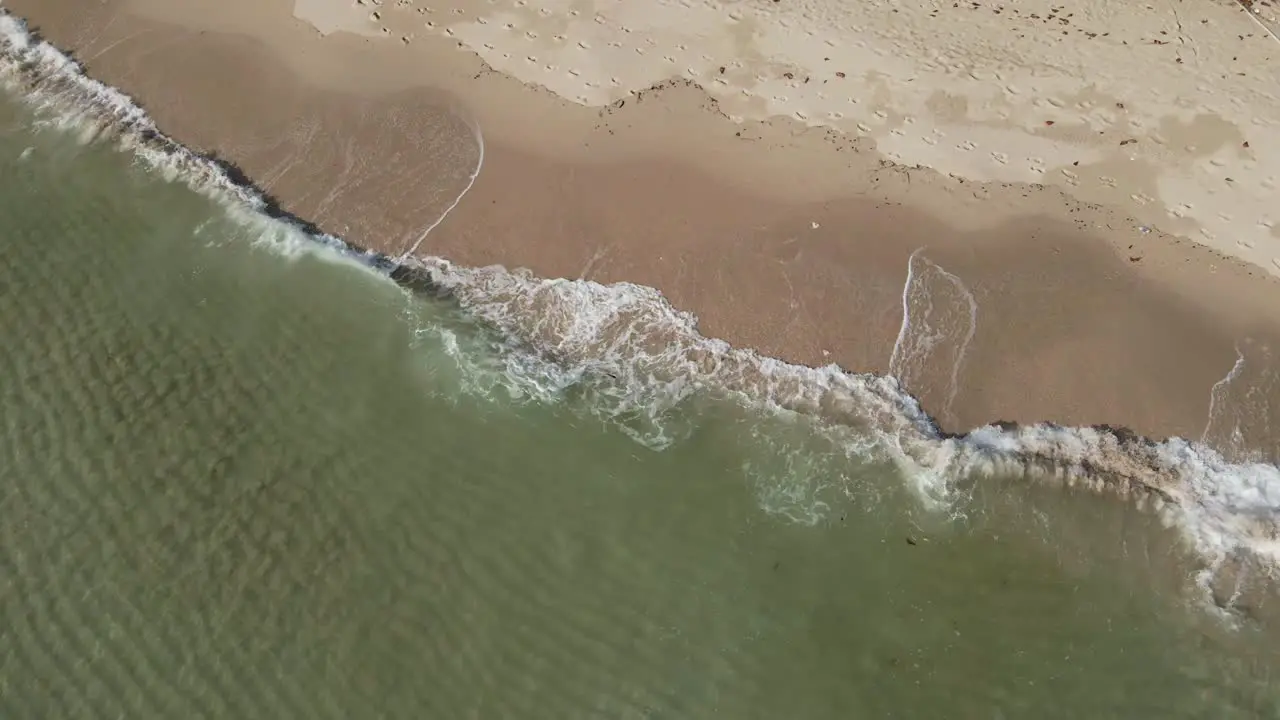 Aerial shot of clear ocean small waves crashing on a white sand beach