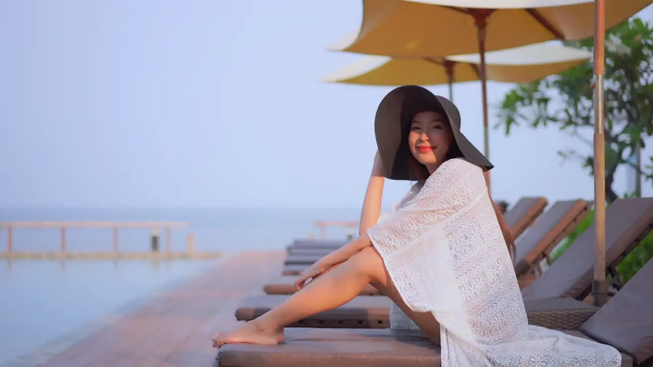 Gorgeous woman in big black hat illuminated by sunset light resting on sunbed