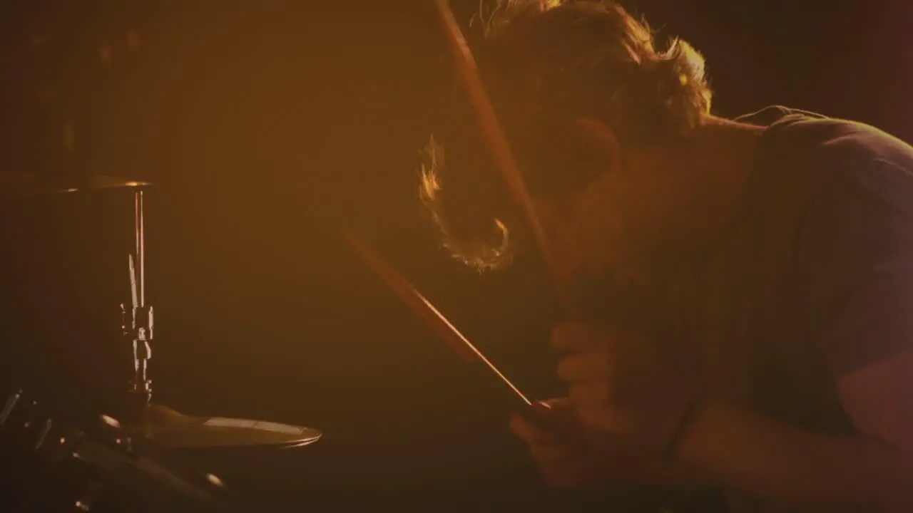 Video of caucasian male drummer playing drum kit under orange coloured lights