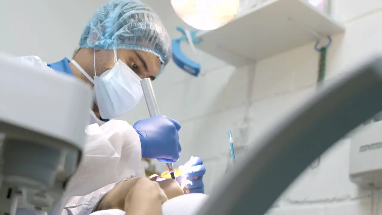 Dentist Doctor Surgeon in a Mask sitting back examining teeth of patient in the Dental Medical Office