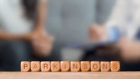 Medical Concept With Wooden Letter Cubes Or Dice Spelling Parkinson's Against Background Of Doctor Talking To Patient