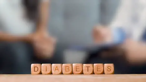 Medical Concept With Wooden Letter Cubes Or Dice Spelling Diabetes Against Background Of Doctor Talking To Patient