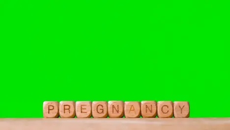 Concept With Wooden Letter Cubes Or Dice Spelling Pregnancy Against Green Screen Background