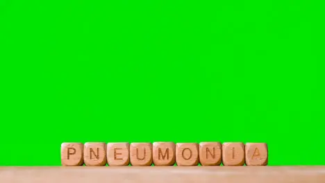 Medical Concept With Wooden Letter Cubes Or Dice Spelling Pneumonia Against Green Screen Background