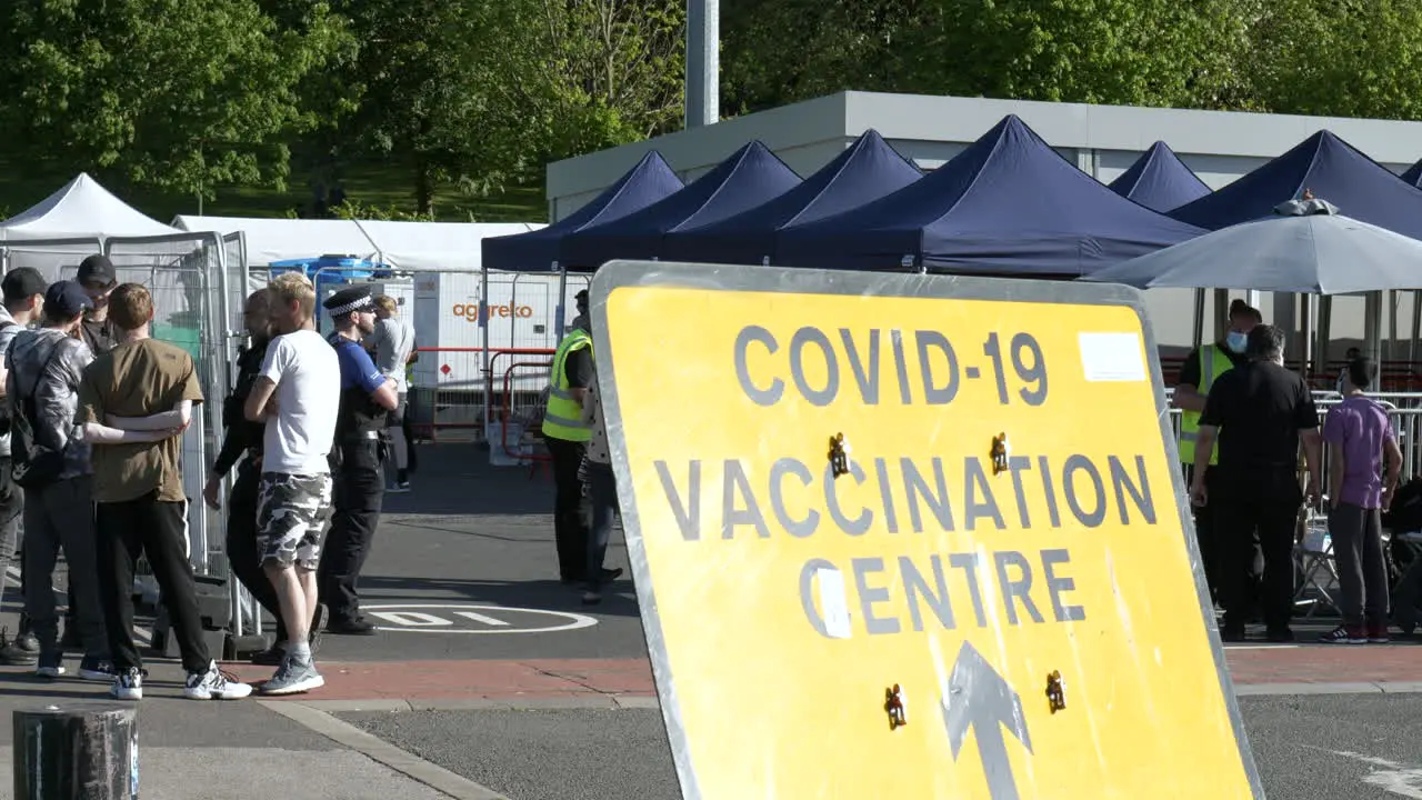 Coronavirus COVID-19 Vaccination Centre Sign with members of the public and officials in the background