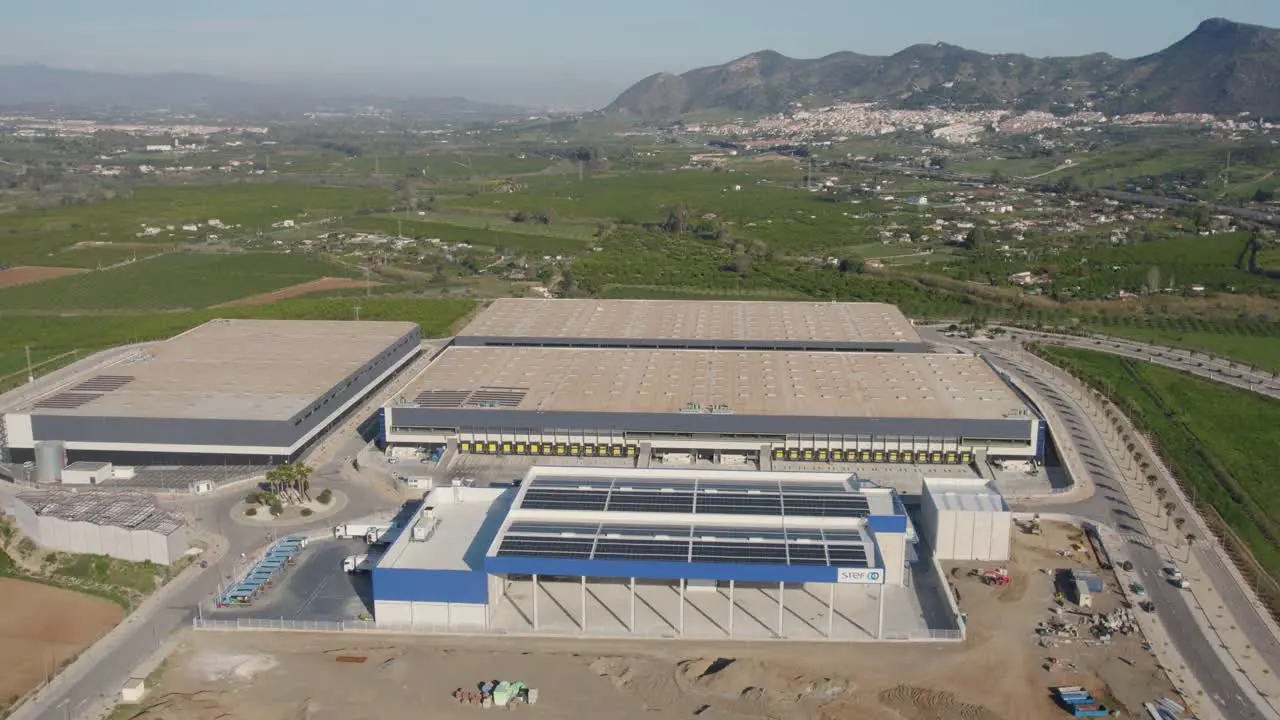 Industrial Warehouses Distribution Center With Mountains and Village in the Background