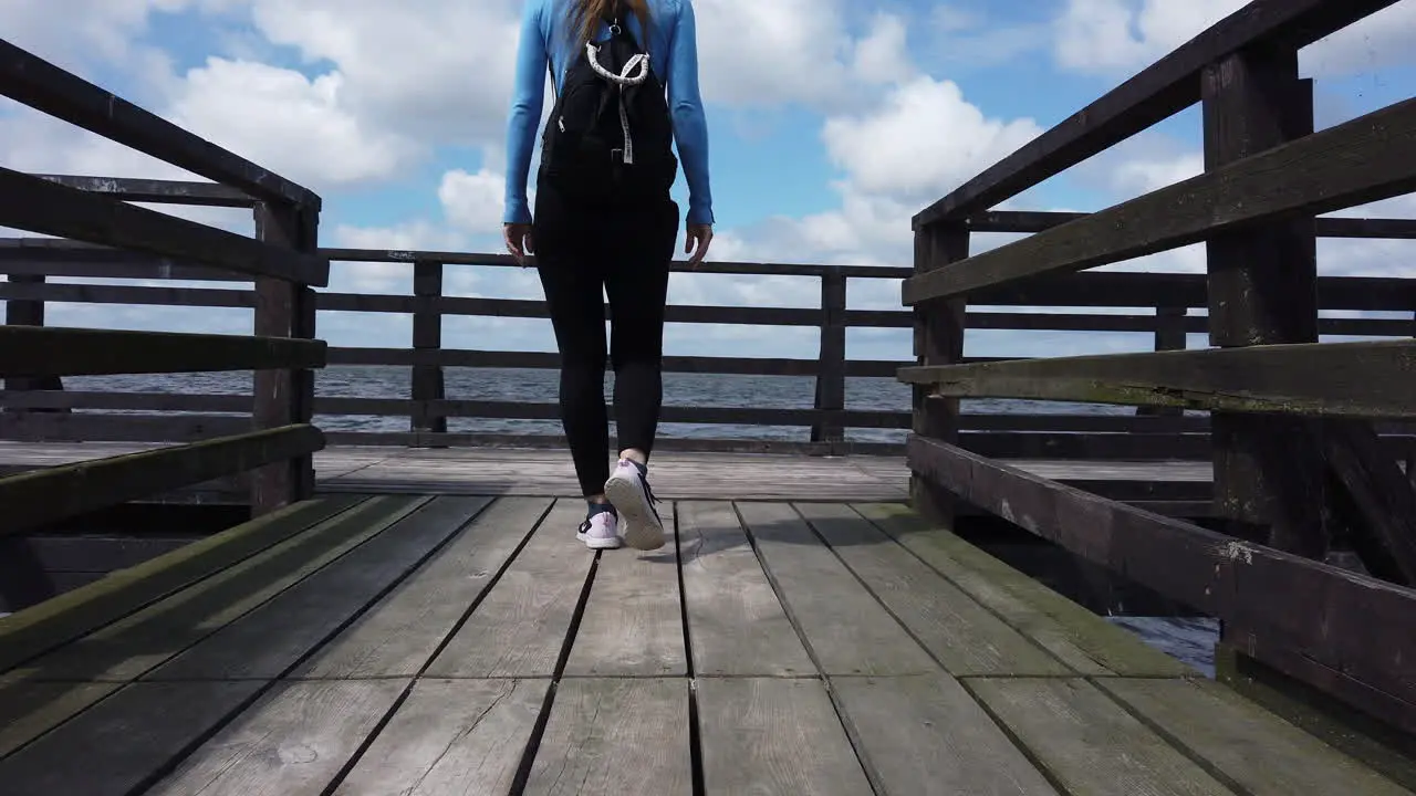 Cinematic shot of a woman walking on a lagoon pier and raising her arms in joy at the end