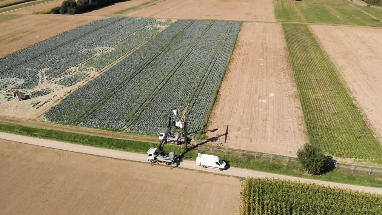 Aerial shot of two electricians on cranes repairing a power line over green fields