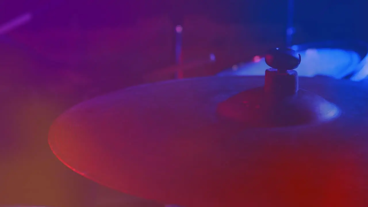 Video of hands of drummer playing drum kit cymbal in foreground red and blue light