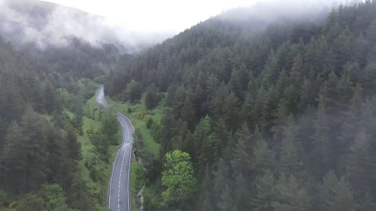 Aerial View Of A Drone Descending From The Clouds To A Humid Mountain Road Crossing A Majestic Pine Forest In The Pyrenees