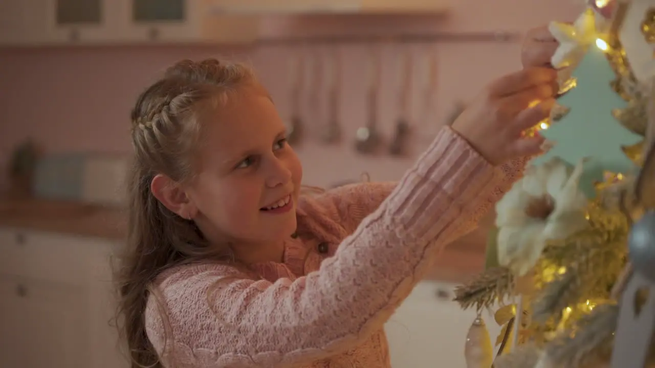 Little Girl Decorates The Christmas Tree With Ornaments At Home