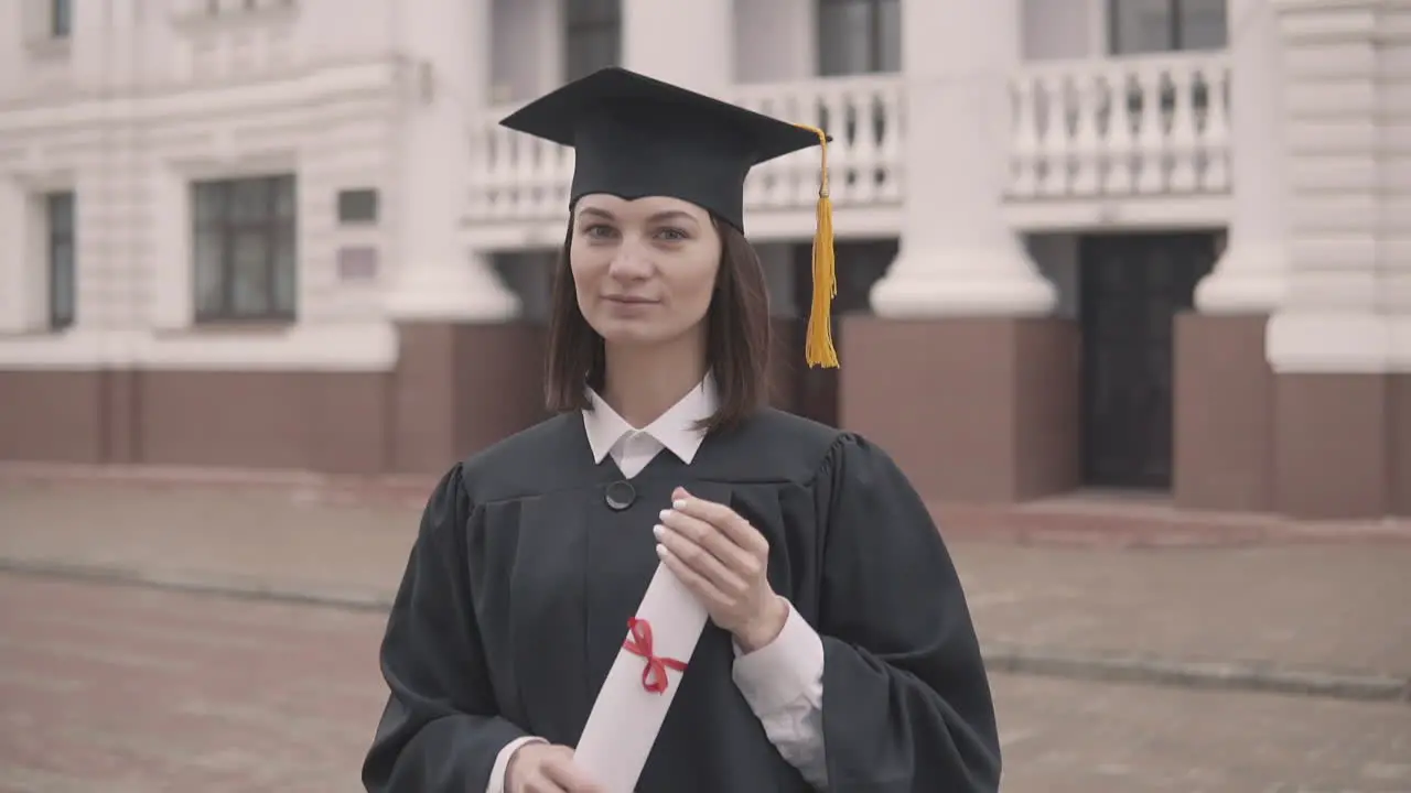 Pretty Girl Graduate Student In Gown And Cap With Diploma Looking At The Camera And Smiling 1